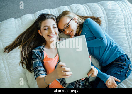 High angle view of happy sisters using tablet computer while lying on bed at home Stock Photo