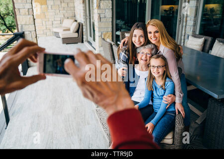Cropped hands of senior man photographing happy family through smart phone on porch Stock Photo