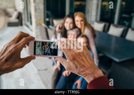 Cropped hands of senior man photographing family through smart phone on porch Stock Photo