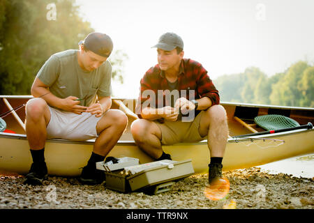 Friends adjusting fishing tackles while sitting on boat against clear sky Stock Photo