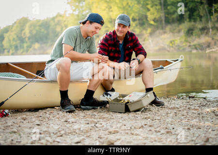 Smiling friends talking while adjusting fishing tackles on boat at lakeshore Stock Photo