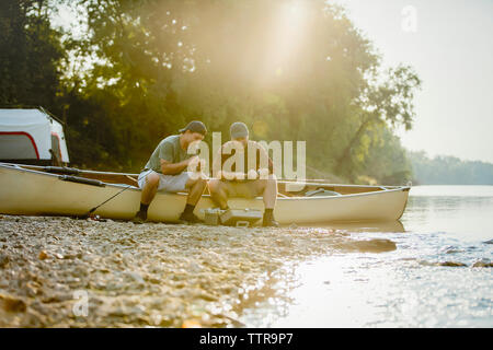 Male friends adjusting fishing tackles while sitting on boat at campsite Stock Photo