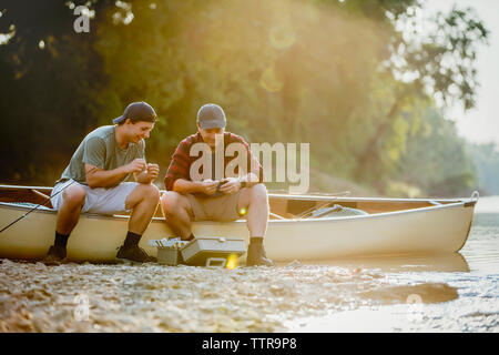 Friends adjusting fishing tackles while sitting on boat by lake Stock Photo