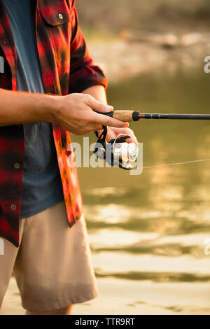 Midsection of mid adult man fishing while standing in lake Stock Photo