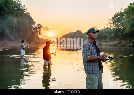 Side view of male friends fishing in lake against sky Stock Photo