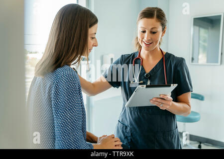 Doctor consoling woman while showing tablet computer in medical examination room Stock Photo