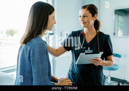 Female doctor consoling woman while holding tablet computer in medical examination room Stock Photo