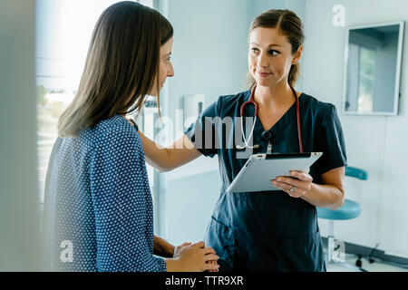 Doctor consoling woman while holding tablet computer in medical examination room Stock Photo