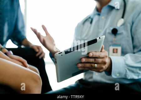 Cropped hand of pediatrician showing tablet computer to mother and daughter in medical examination room Stock Photo