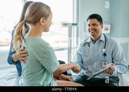 Happy pediatrician shaking hands with girl sitting by mother in hospital Stock Photo
