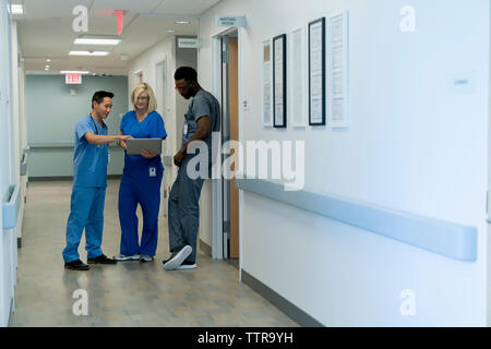 Doctors discussing over laptop computer while standing in hospital corridor Stock Photo