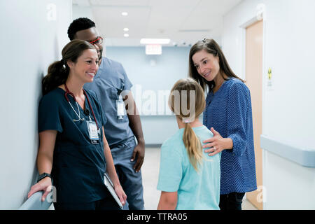 Doctors looking at surprised mother talking with daughter in hospital corridor Stock Photo