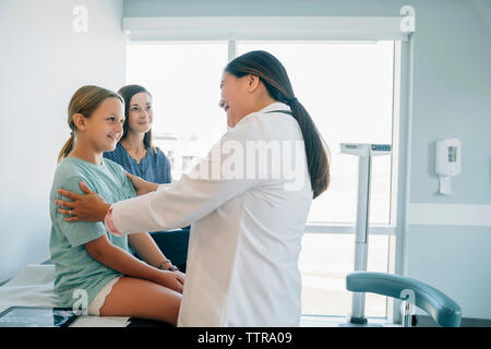 Cheerful pediatrician talking with patient sitting by mother in medical examination room Stock Photo