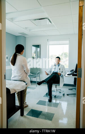 Doctor discussing with female colleague while working in examination room seen through doorway Stock Photo