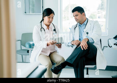 Doctors discussing over tablet computer while sitting in examination room Stock Photo