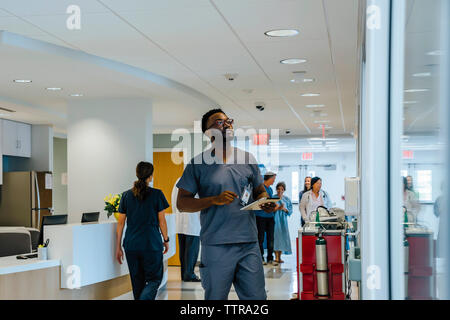 Doctor holding tablet computer while looking away with colleagues working in background Stock Photo