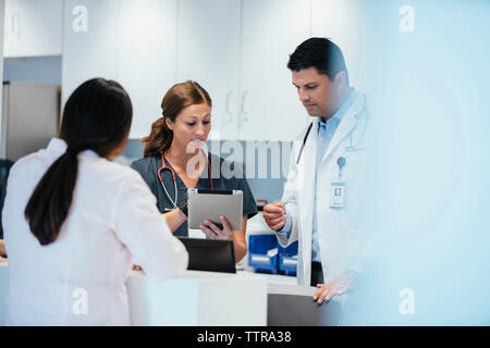 Nurse showing tablet computer to colleague with female doctor standing in foreground Stock Photo