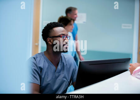 Doctor working at hospital reception with colleagues in background Stock Photo