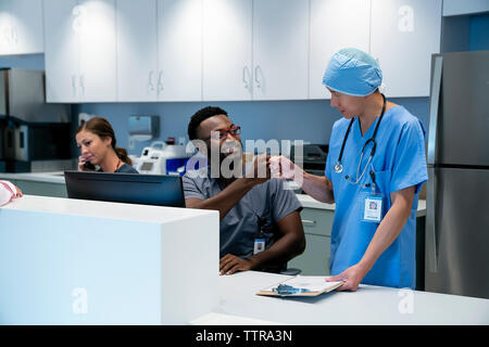 Doctors bumping fists while female colleague talking on telephone at hospital reception Stock Photo