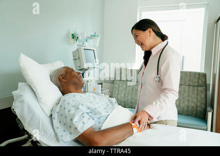 Cheerful doctor talking with senior patient lying on bed in hospital ward Stock Photo