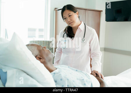Female doctor looking at senior patient lying on bed in hospital ward Stock Photo