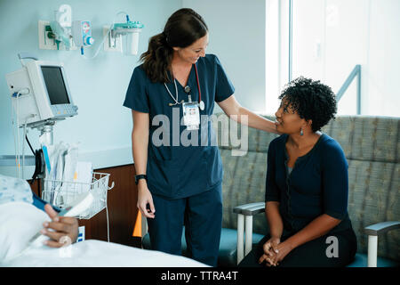 Cheerful nurse talking with woman while senior patient lying in hospital ward Stock Photo