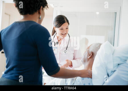 Female doctor talking with senior patient lying by daughter in hospital ward Stock Photo