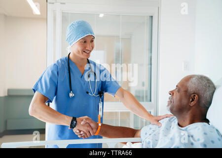 Confident surgeon shaking hands with senior patient in hospital ward Stock Photo