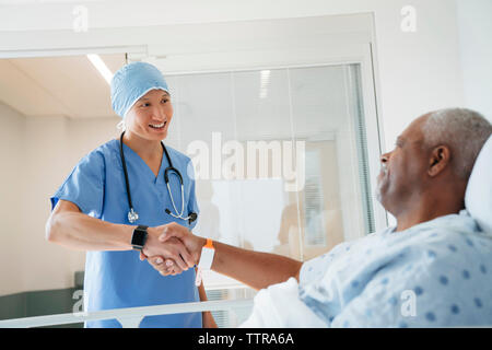 Confident surgeon shaking hands with senior patient lying in hospital ward