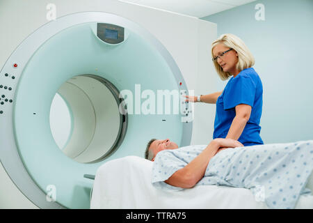 Nurse looking at patient lying on MRI Scanner while pressing start button in examination room Stock Photo