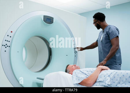 Male nurse adjusting button on MRI Scanner while patient lying in examination room Stock Photo