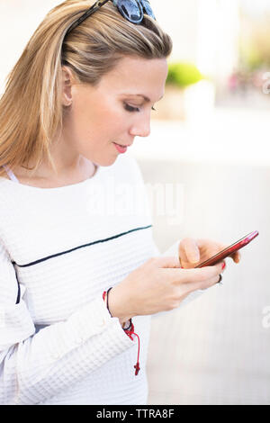 Woman using mobile phone while standing on footpath Stock Photo