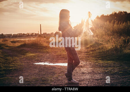 Girl holding kite and standing on field against sky on sunny day Stock Photo