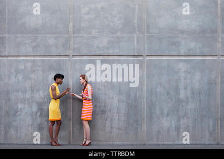 Full length of multi-ethnic friends talking while standing against wall Stock Photo
