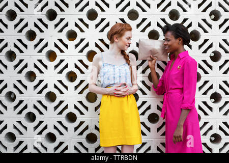 Multi-ethnic friends talking while standing against patterned wall Stock Photo