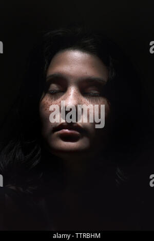 Close-up of teenage girl with eyes closed against black background Stock Photo