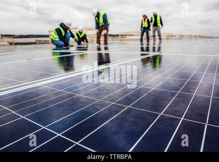 Workers working on solar panel field against cloudy sky Stock Photo