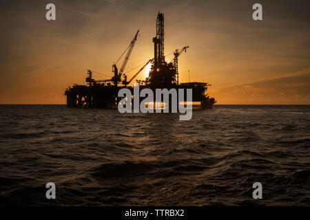 Oil rig in sea against sky during sunset Stock Photo