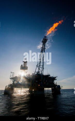 Oil rig in sea emitting fire on sunny day Stock Photo