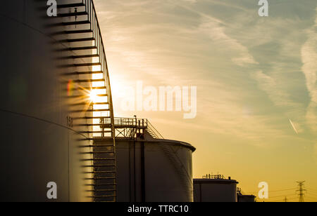 Low angle view of storage tanks at oil refinery against sky during sunset Stock Photo