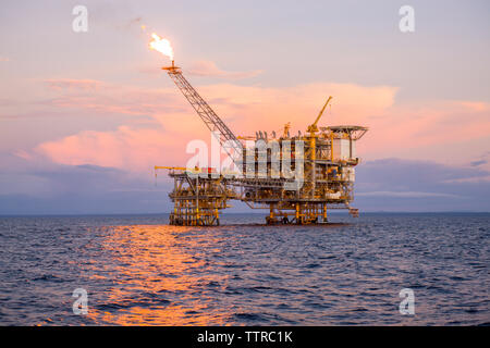 Offshore platform in sea against sky during sunset