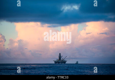 View of drilling rig in sea against cloudy sky during sunset Stock Photo