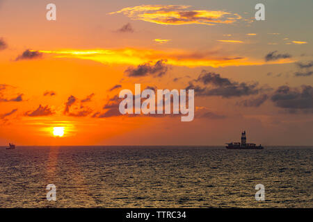 Distant view of drilling rig in sea against cloudy sky during sunset Stock Photo