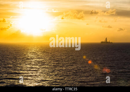 Distant view of drilling rig in sea against sky during sunset Stock Photo