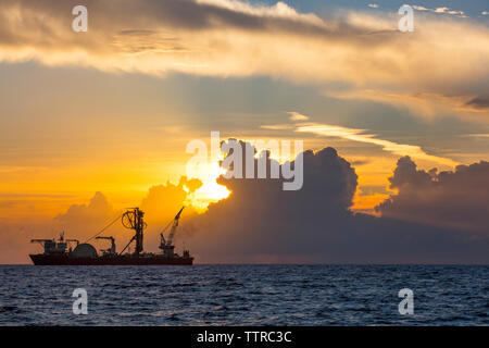 Machineries on ship in sea against cloudy sky during sunset Stock Photo