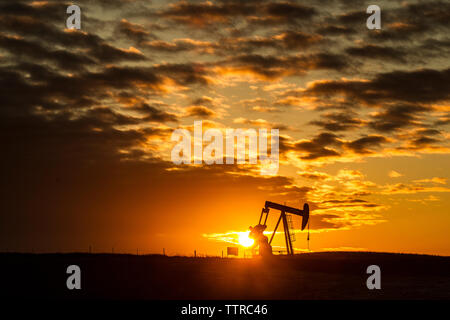 Mid distance view of silhouette pumpjack at oil industry against cloudy sky during sunset Stock Photo