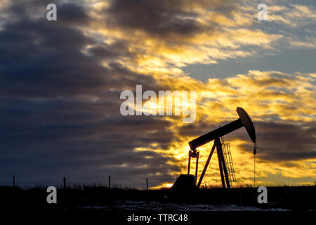 Pumpjack at oil industry against cloudy sky during sunset Stock Photo