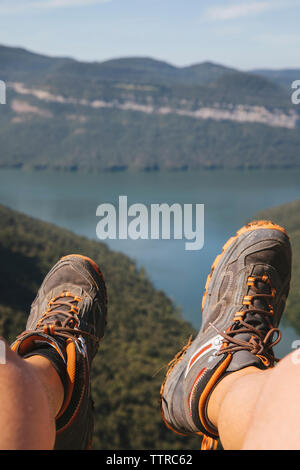 Low section of male hiker sitting on mountain against lake Stock Photo