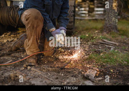 Low section of worker welding while kneeling on field Stock Photo