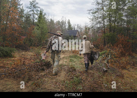 Rear view of boy carrying dead turkey while walking with father on field Stock Photo